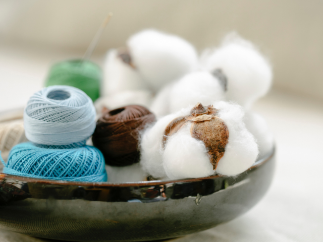 Various balls of multicolored threads next to white cotton in a bowl. 