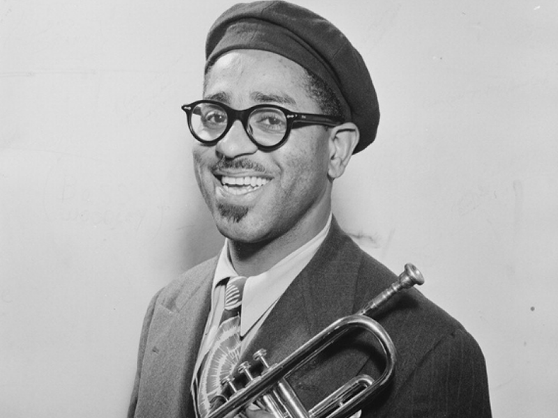 A smiling Dizzy Gillespie holding a trumpet and wearing dark glasses and a beret 