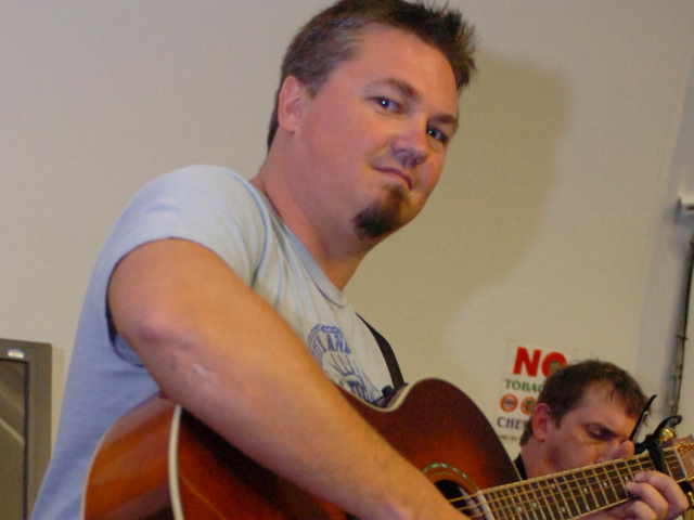 Edwin McCain wearing a light gray shirt and holding a brown guitar. 