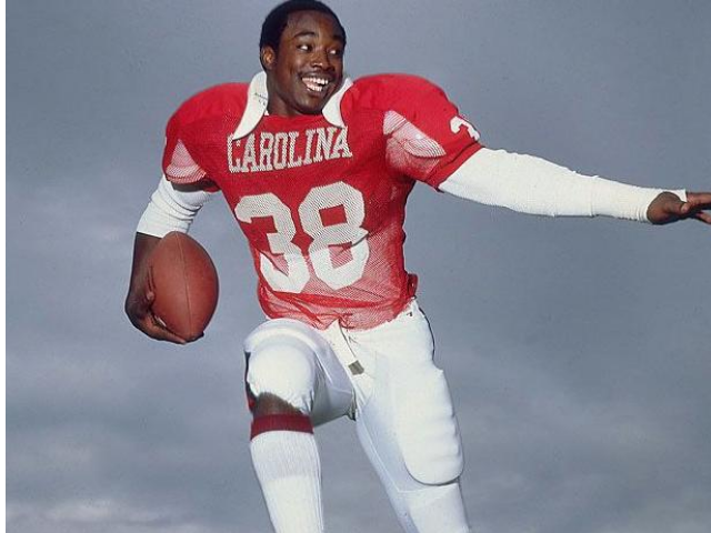 George Rogers in a red and white football uniform holding a football.