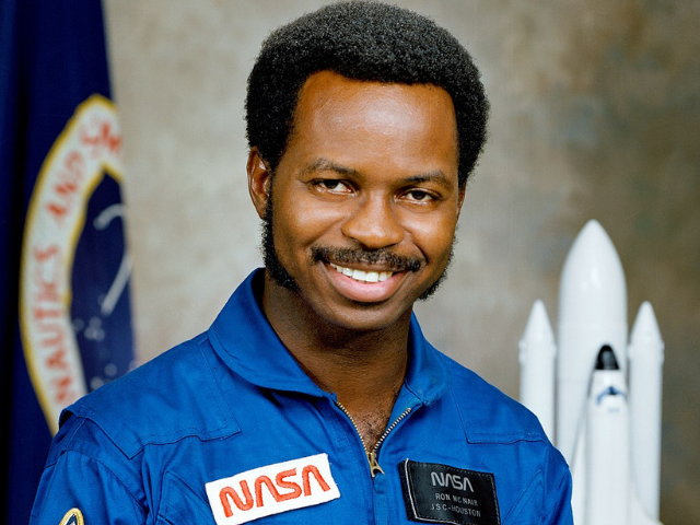 A smiling Ronald McNair wearing a blue Nasa space jumpsuit.