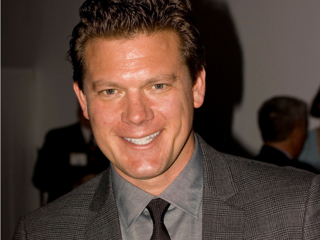 A smiling Tyler Florence wearing a grey and black suit.