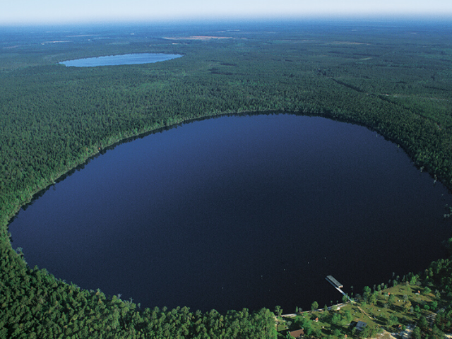A large circular body of water tucked in between a forest of trees. 
