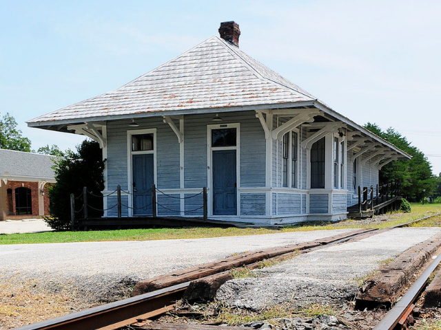 a light blue building with a whitish-gray roof next to a railroad track. 