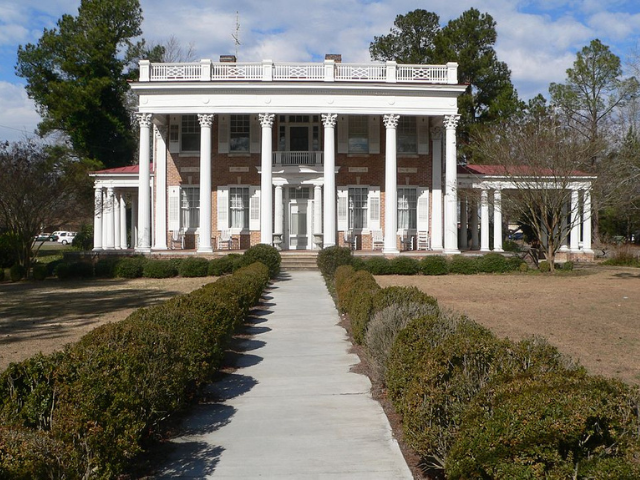 A brick house with large white prominent columns in the front of the house.  