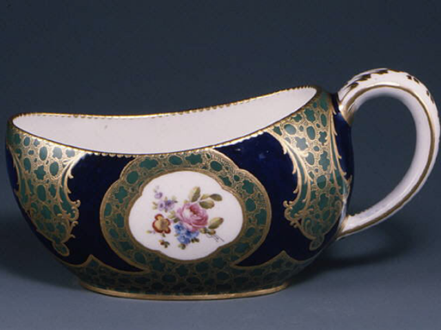 An intricately designed chamber pot in dark blue, gold, teal, and white with a flower motif in center. 