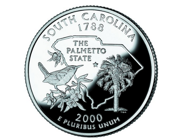 A silver coin with a map of South Carolina, the palmetto tree, and the Carolina wren. 