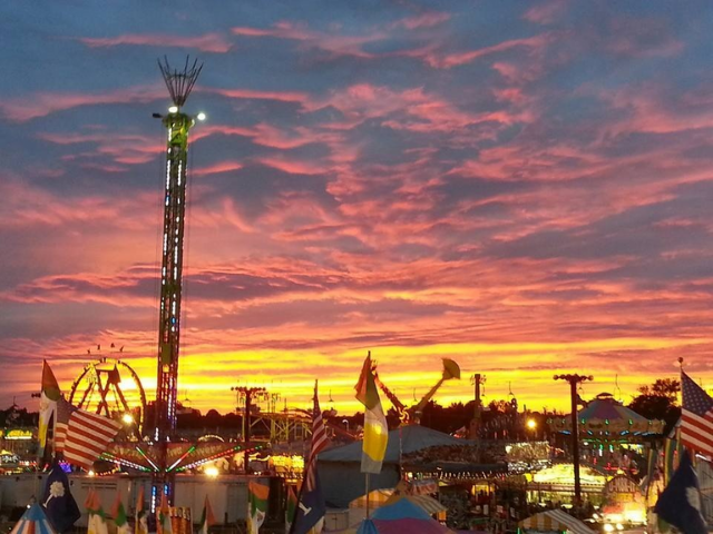 Lit up fair rides against a yellow, pink, and purple sunset. 