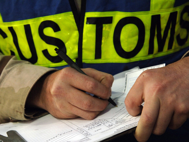 A person wearing a blue and yellow-green customs vest writing something on clipboard. 