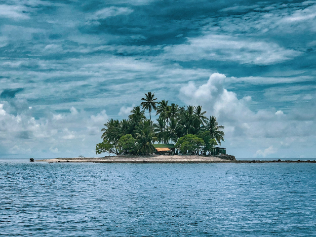 island with green trees against a blue sky with white clouds. 