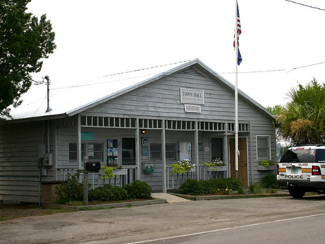 A grey building with a white gabled roof and an American flag standing in front