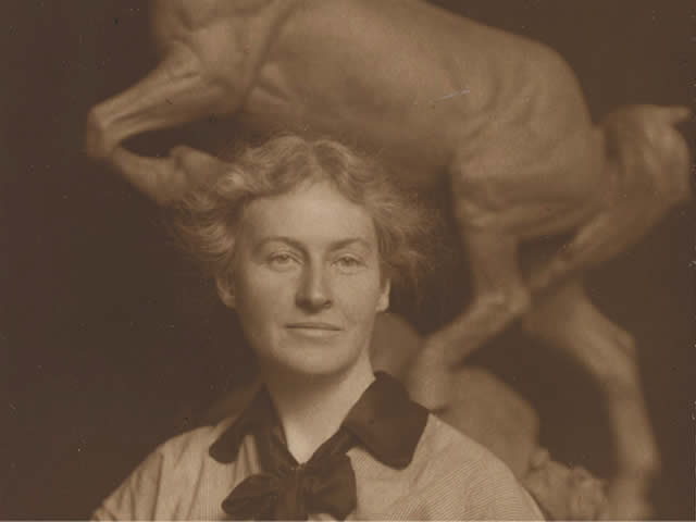 Anna Hyatt Huntington standing in front of horse sculpture.