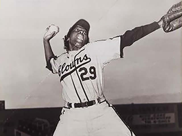 Mamie wearing a baseball uniform and pitching. 