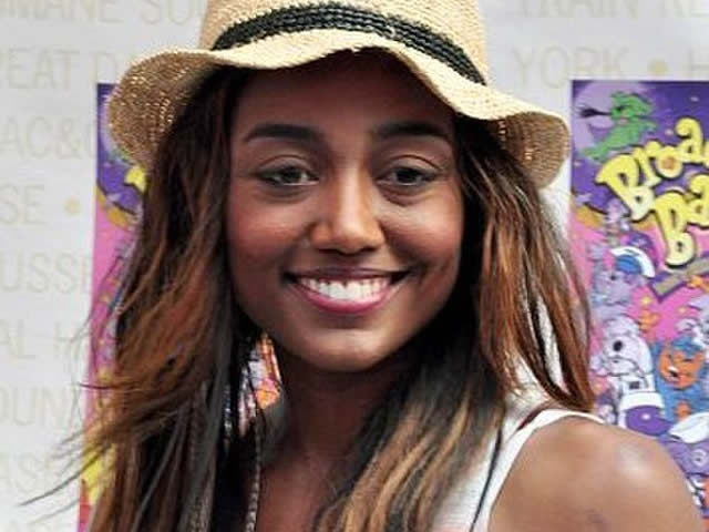 A smiling Patina Miller wearing a straw hat and pastel colored tank top