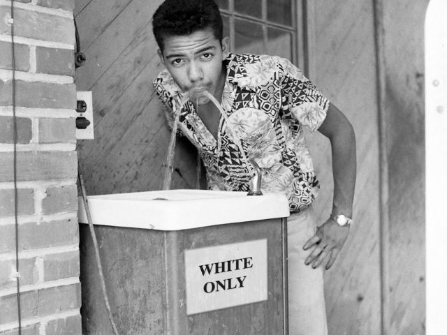Cecil Williams drinking from a water fountain labeled Whites Only