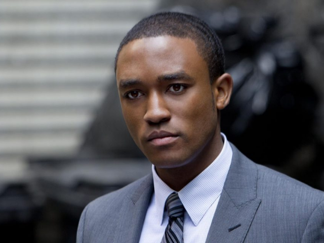 A young Black man in a gray suit, white dress shirt, and patterned tie.