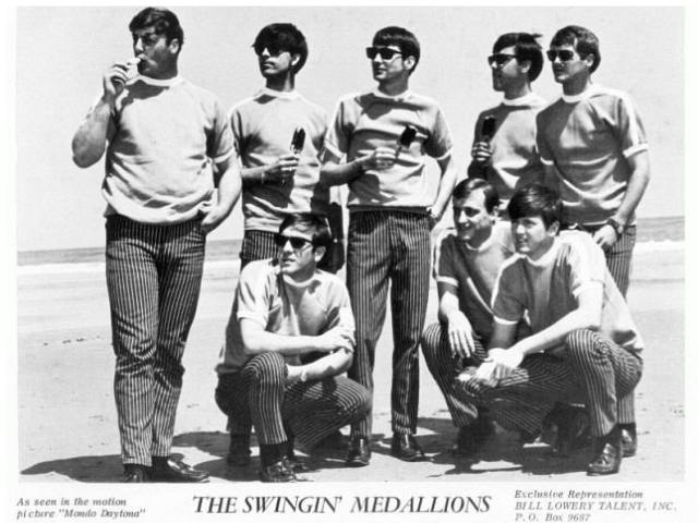 A group of young men posing together on a beach. 