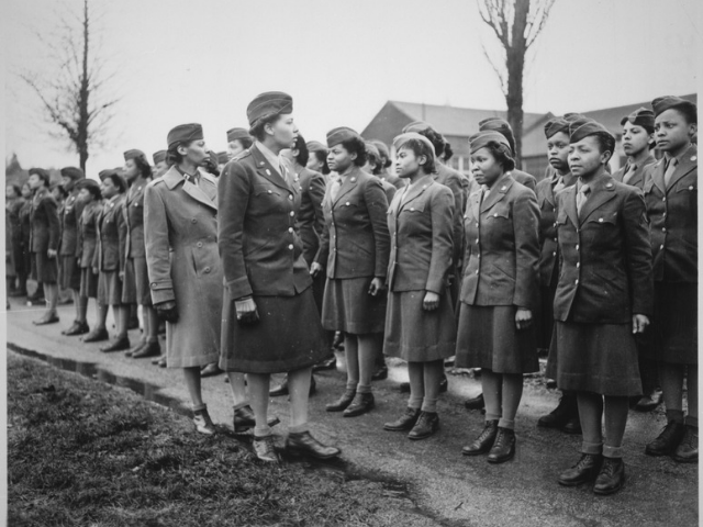Women in military uniform being inspected by two women. 