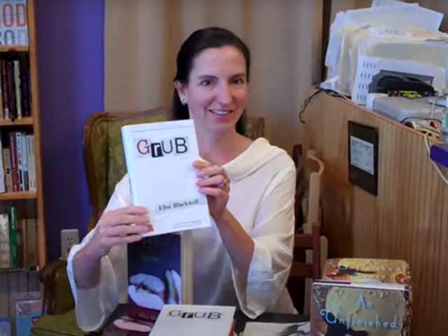 Color photograph of Elise Blackwell holding a copy of her book titled Grub