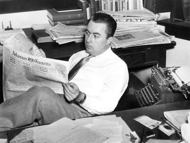 Black and white photograph of Harry Ashmore leaned back in a chair reading the newspaper.