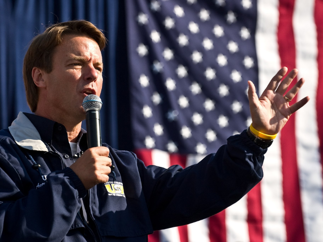 Color photograph of John Edwards standing in front of an American flag