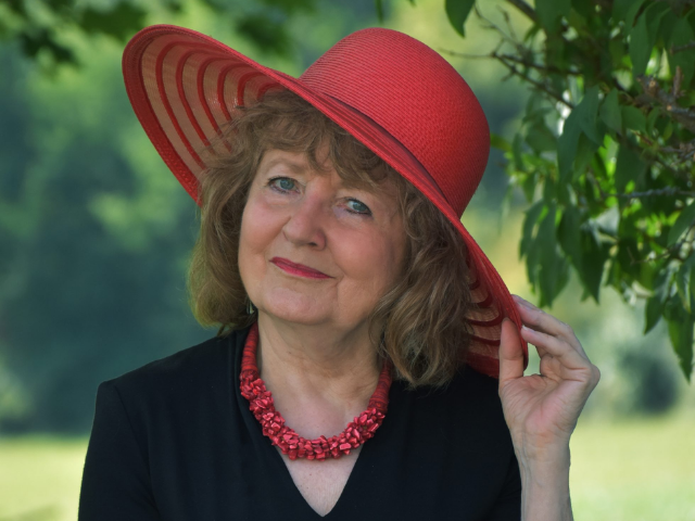 Photograph of Susan Ludvigson wearing red hat, red necklace, black top, smiling