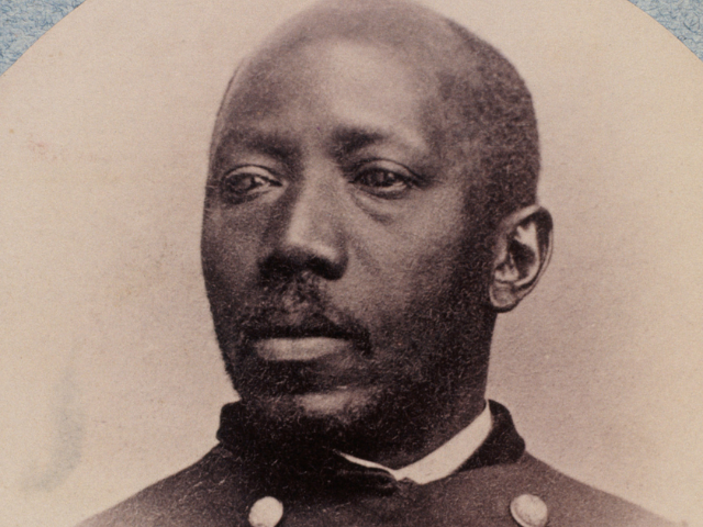 A black man with a receding hairline and mustache goatee. 